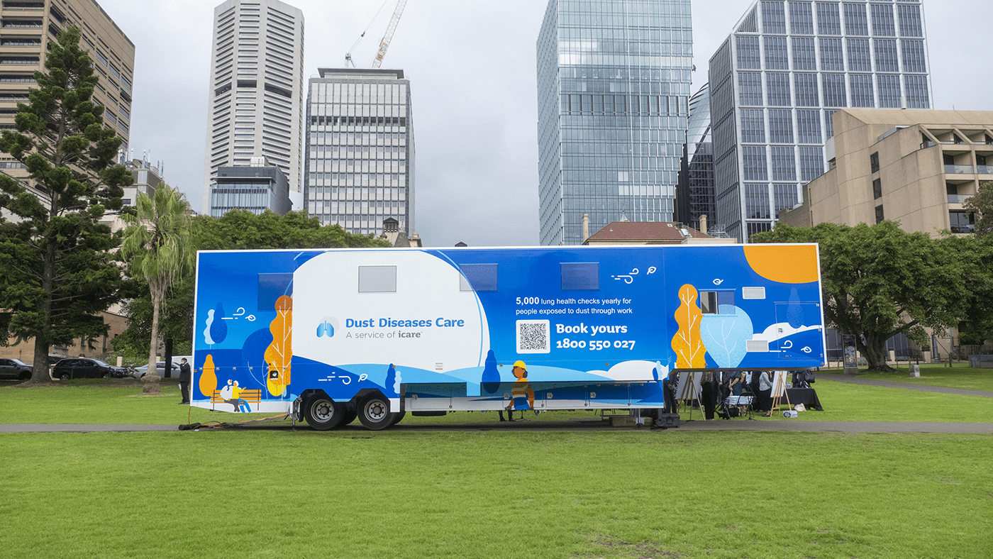Photo of the outside of the icare Mobile Lung Bus parked in The Domain with Sydney CBD in the background. Text on the lung bus reads Dust Diseases Care: A service of icare. Book yours 1800 550 027
