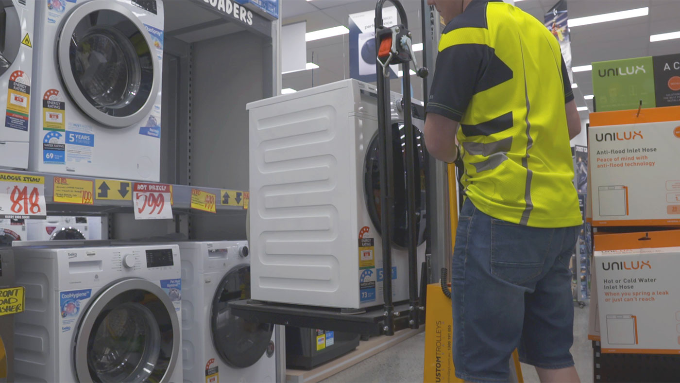 Worker using trolley to lift washing machine onto shelf