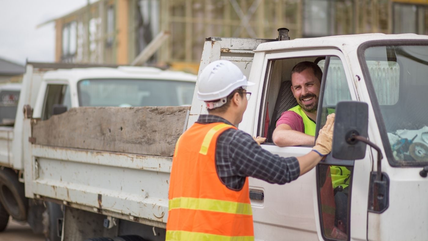 Construction worker driving a ute while talking to his workmate