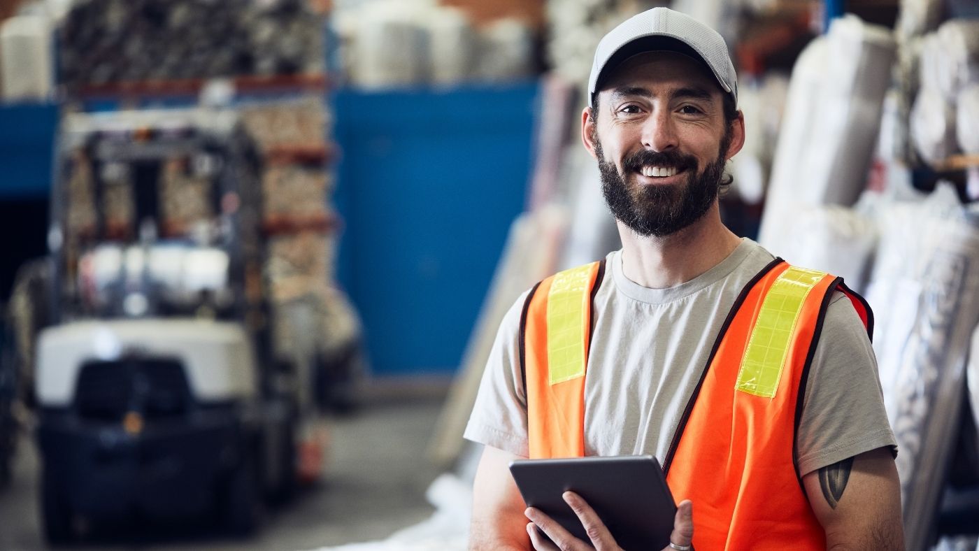 A man in a warehouse wearing a safety vest and holding a tablet