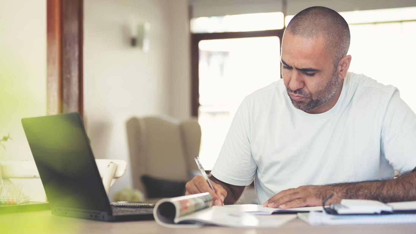 Mature man working on a laptop and writing notes.