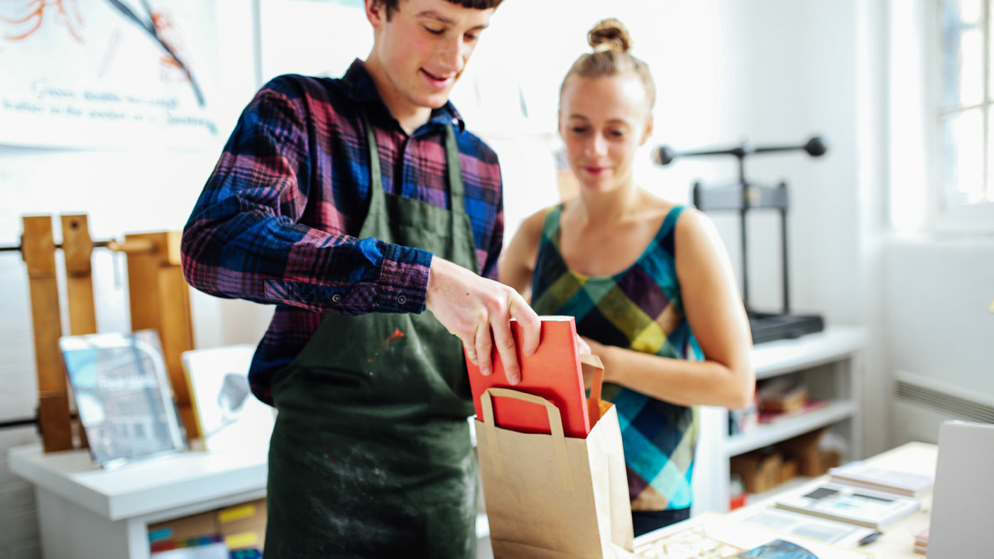 A worker places a book in a bag while a colleague looks on in a book store.