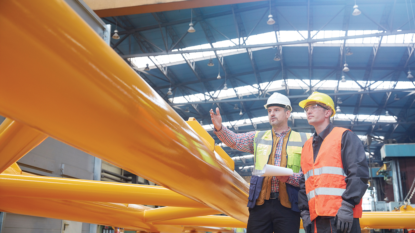 Two men in safety wear discuss a project in a factory setting.