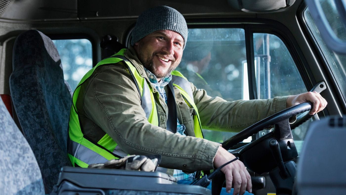 Smiling male truck driver sitting in a truck wearing a beanie and high visibility vest