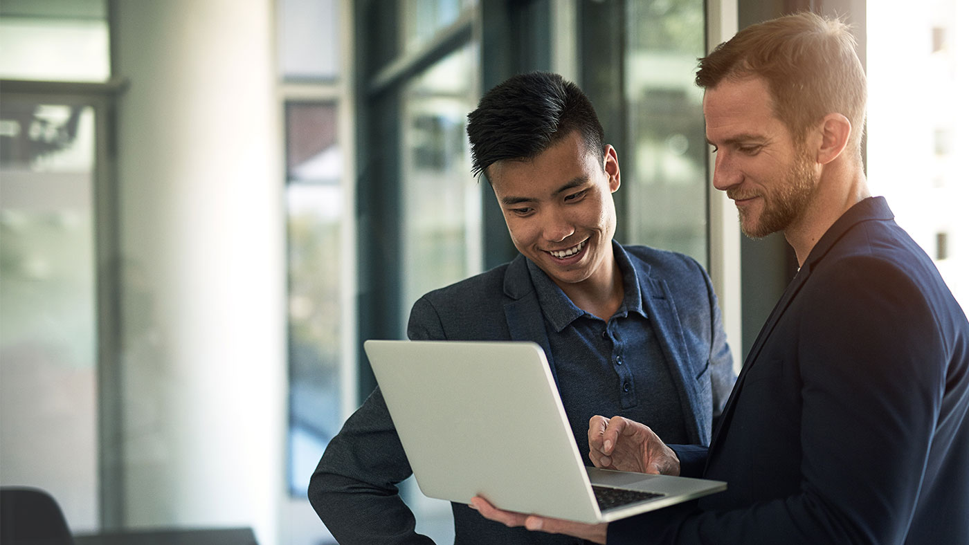 two men standing up looking at a laptop in an office