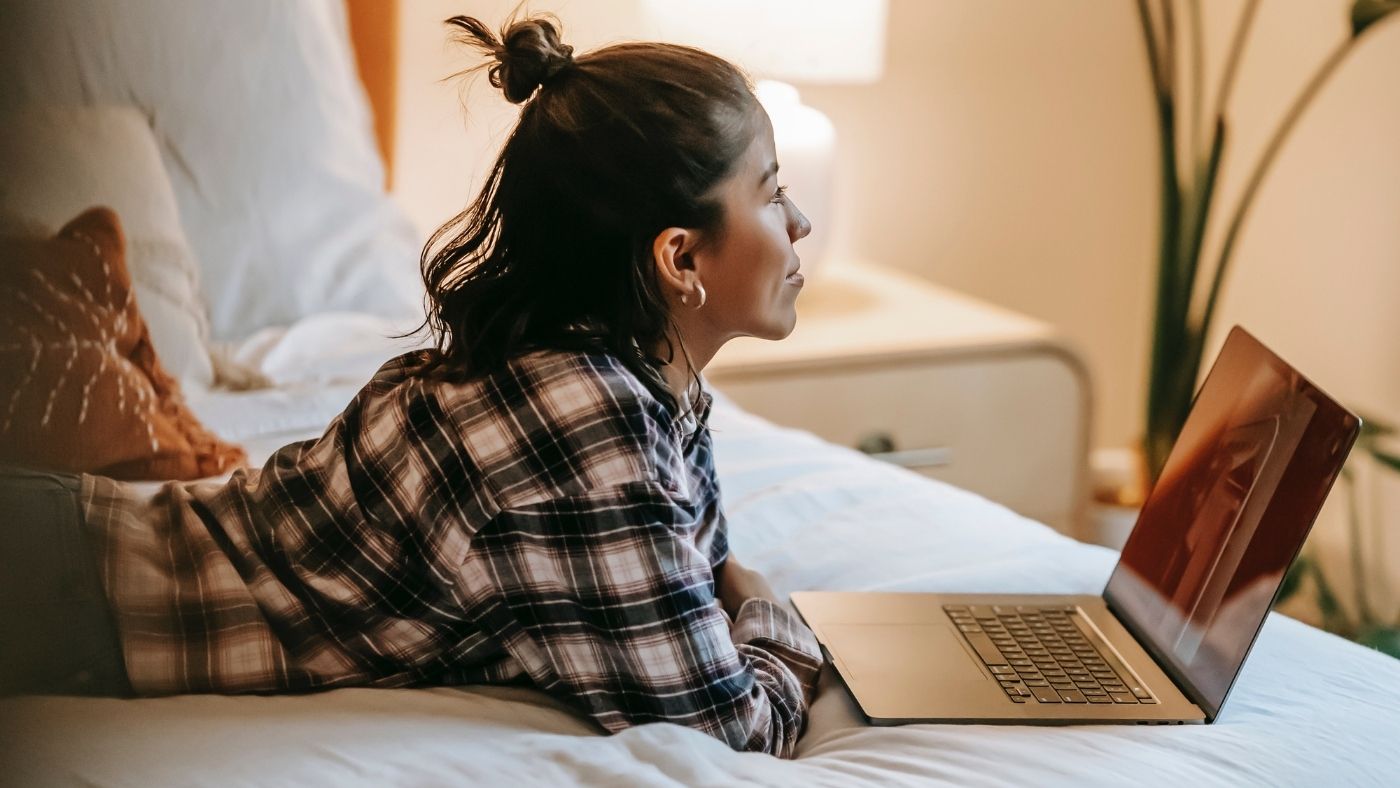 Female employee working from home on her bed with laptop