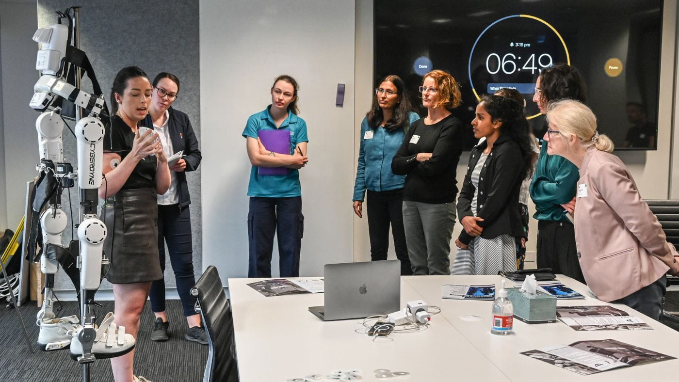 A female presenter presents various assistive technology solutions to a group of staff.