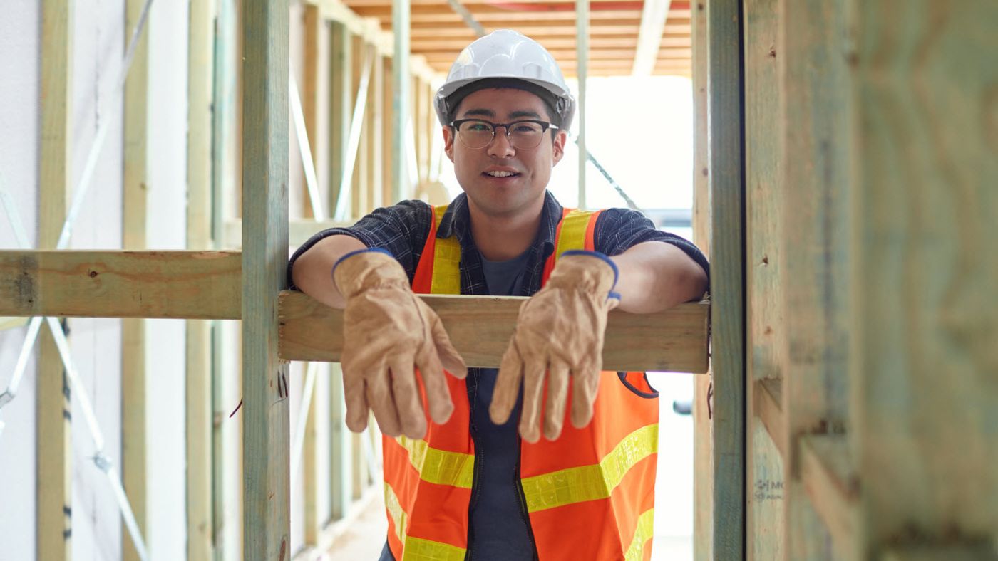 Construction worker wearing a white protective helmet, leans on a wooden beam