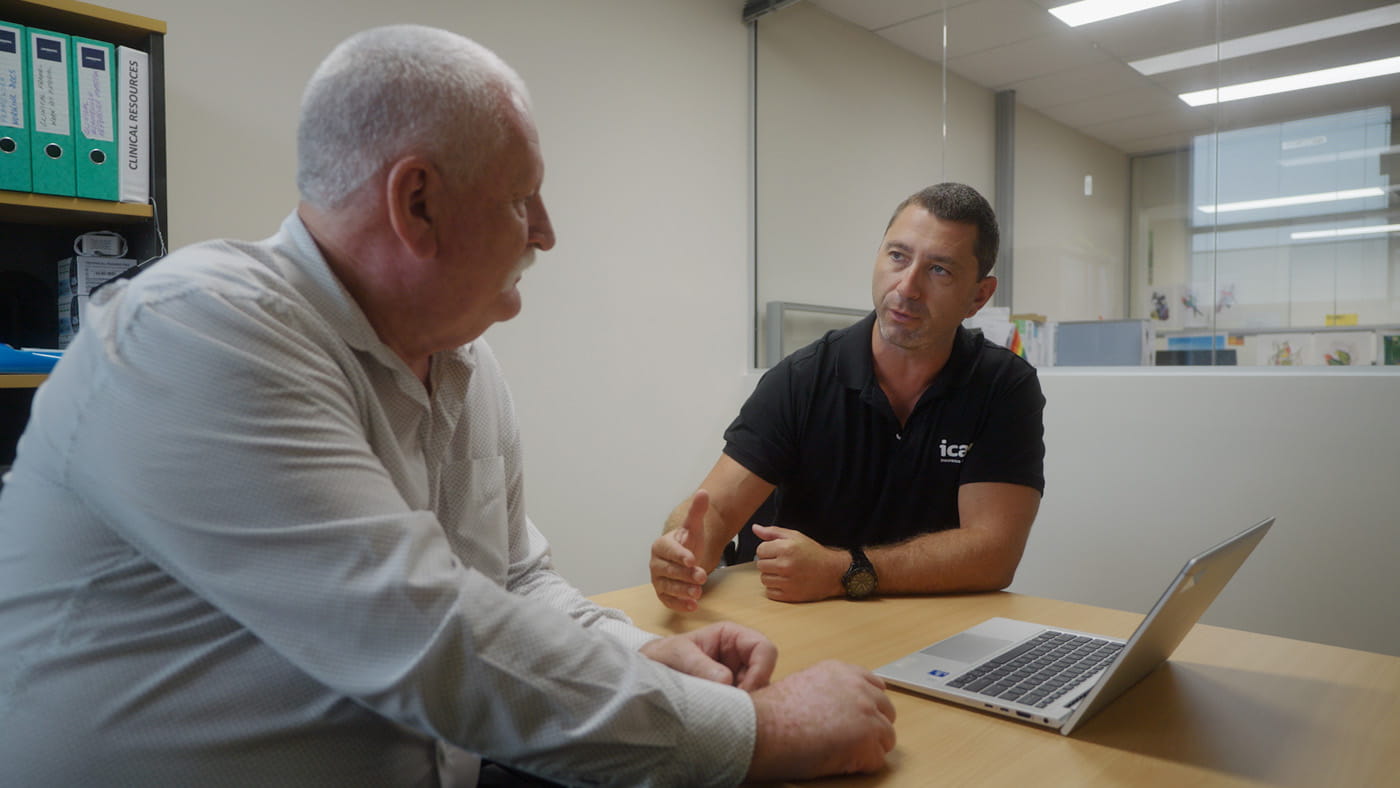 Image of man in icare polo shirt sitting in an office talking to another man