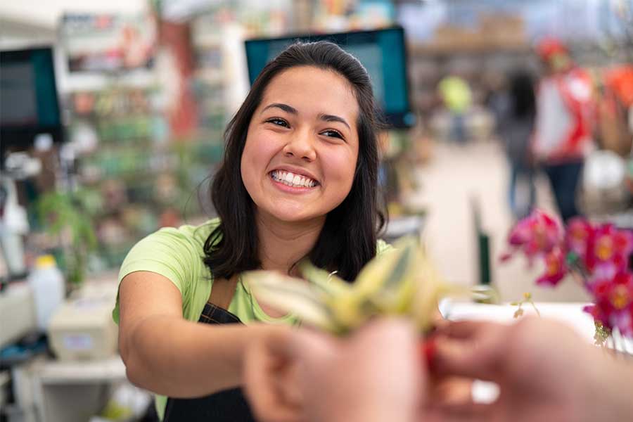 A-woman-smiling-at-the-camera-handing-back-change-working-in-a-garden-centre-900x600 A woman smiling at the camera handing back change in a garden centre.
