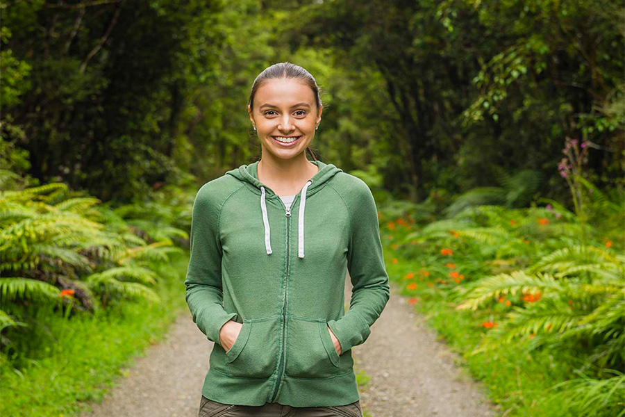 A woman smiling at the camera in a Forrest.
