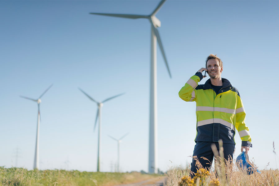 Smiling engineer standing in a field at a wind farm talking on cell phone