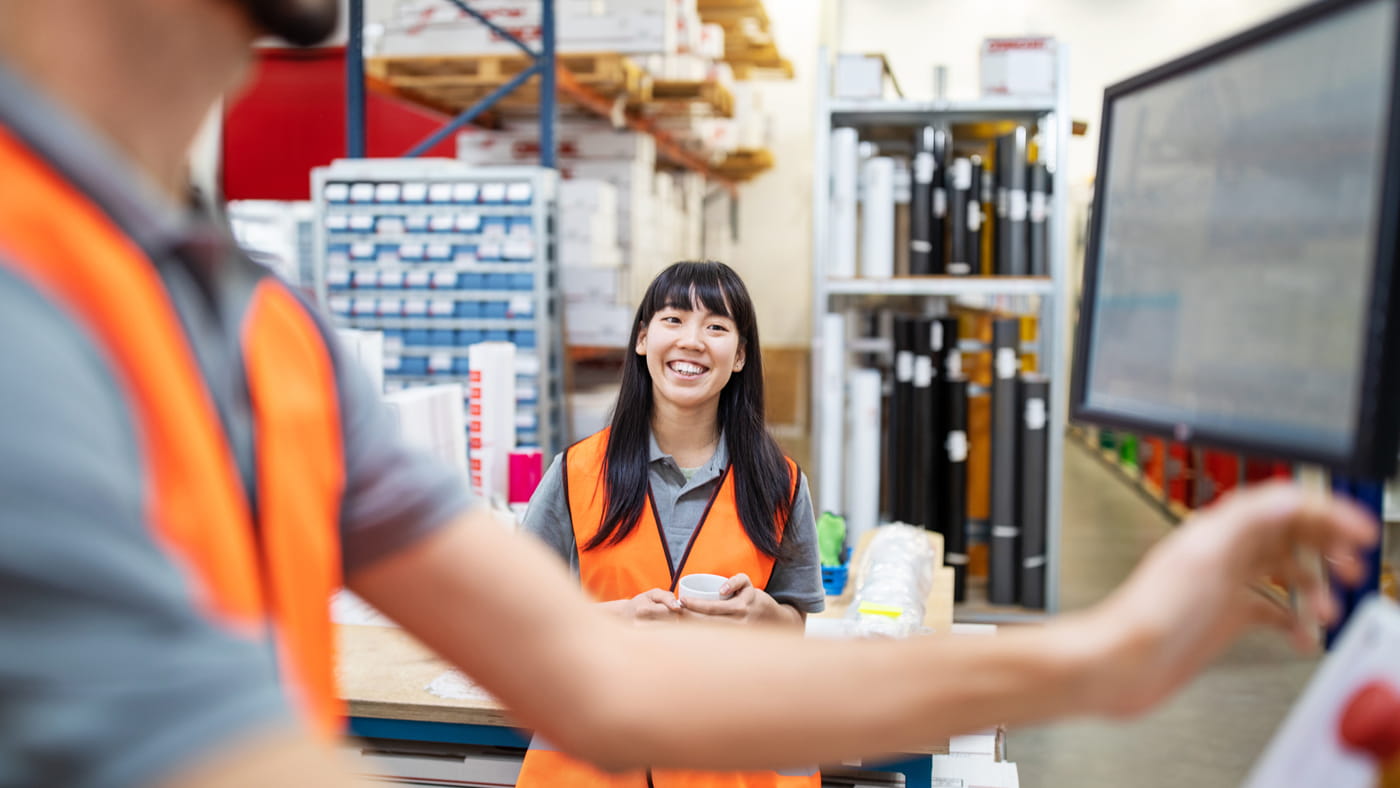 A woman in hi vis smiles at her colleague in a manufacturing warehouse.