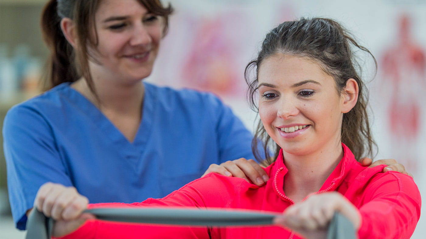 A female healthcare worker helping a female patient stretch with a band.