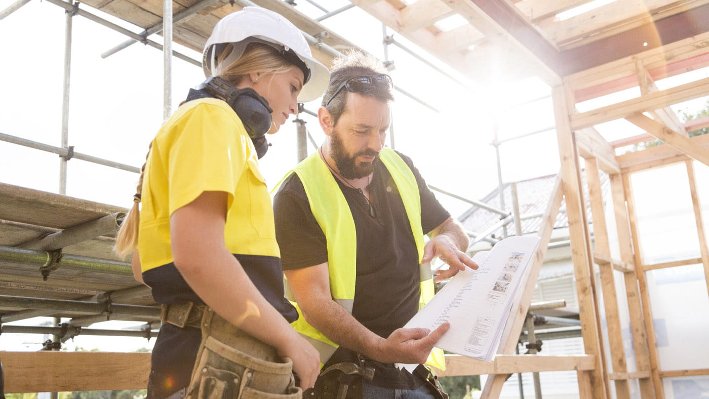 male and female construction workers look at plans on site.