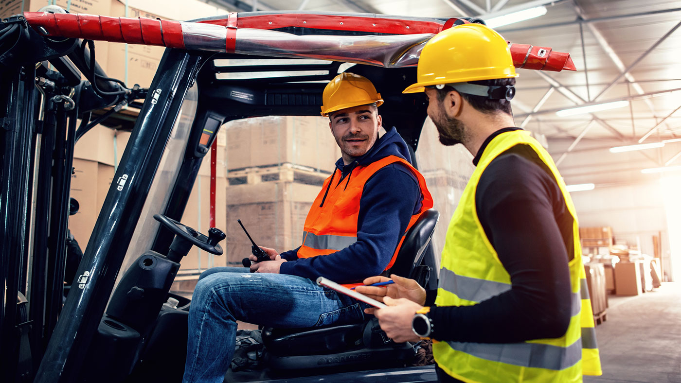 Two male workers in warehouse with forklift.