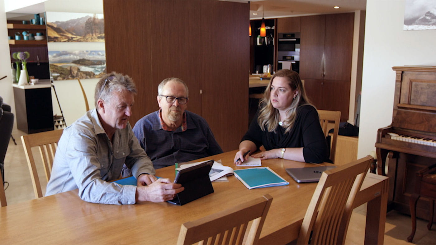 two males and one female sitting at a table looking at a tablet device