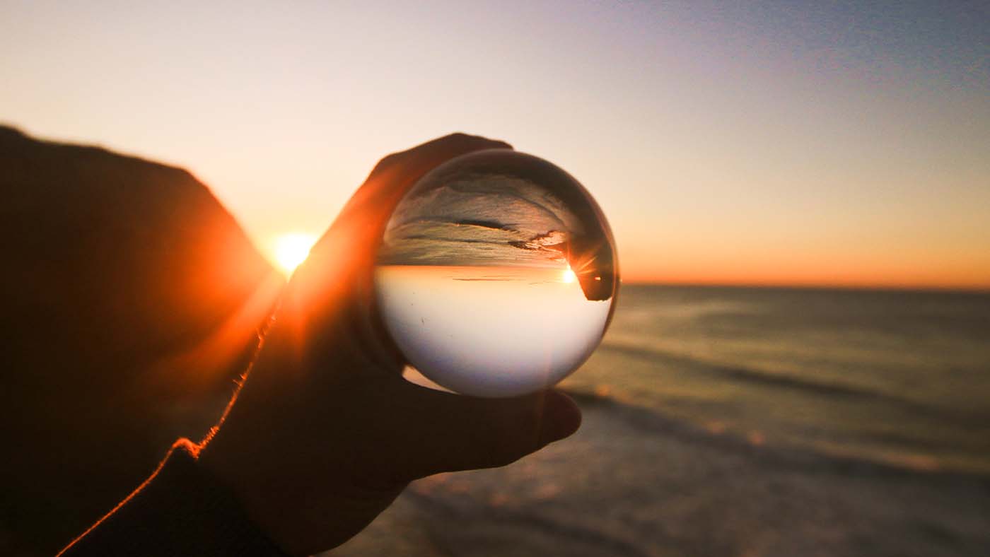 A photograph of the beach at sunset with a hand holding a glass ball by Shine Art Prize entrant Tommy Hawthorne
