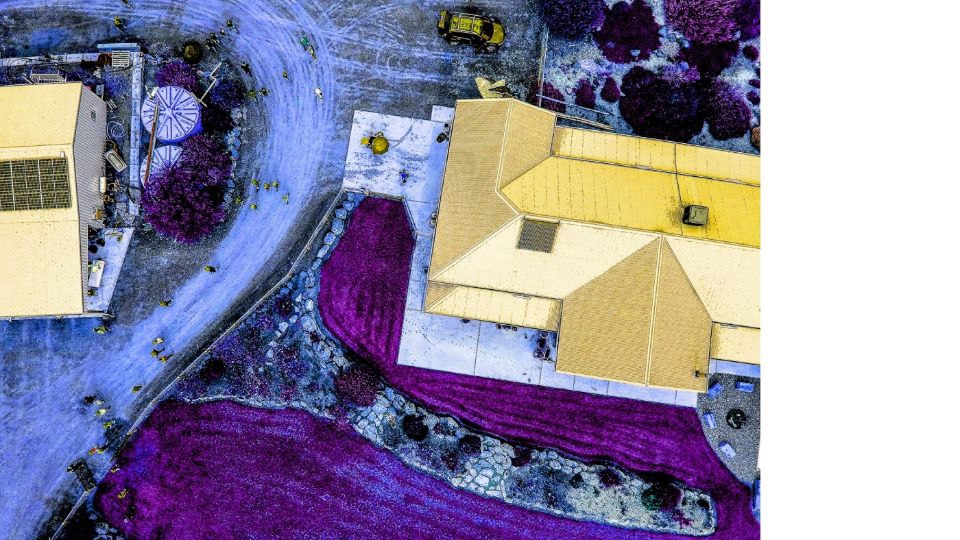 Aerial drone photograph of two buildings with yellow roofs. The surrounding areas have snow on the floor and bright purple areas surrounding the building