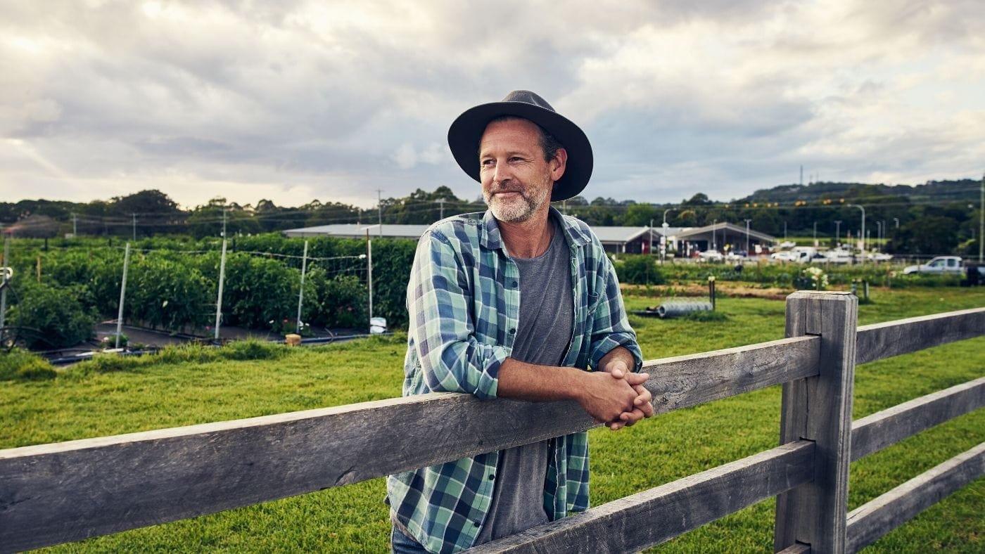 Farmer standing at a fence on a farm looking into distance