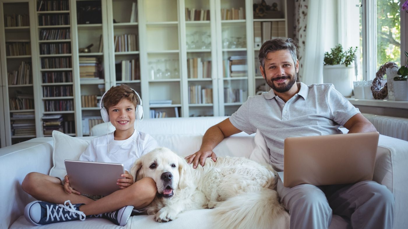 Man sitting on couch with dog and son working from home